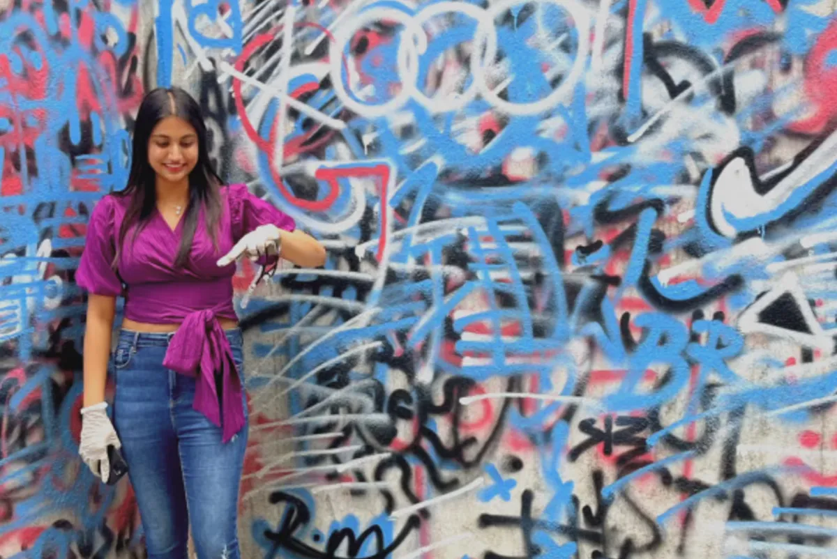 Nanditha in front of a wall covered in graffiti.