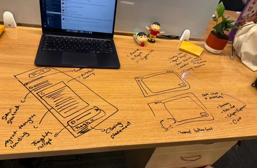 Wireframes sketched in marker directly on a wooden desk, next to a laptop.